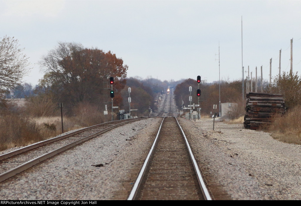 An approaching westbound grain train approaches in the distance as the signals at Smithshire clear the way for an eastbound to cross over in front of it